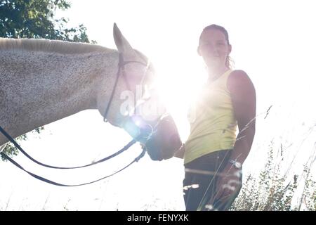 Portrait of woman with grey horse against sunlit sky Stock Photo