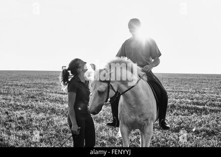 B&W image of woman chatting with man riding grey horse in field