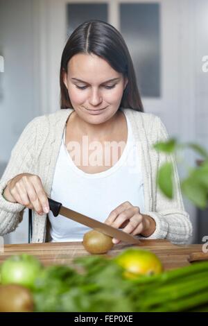 Woman cutting green kiwi on wooden table Stock Photo