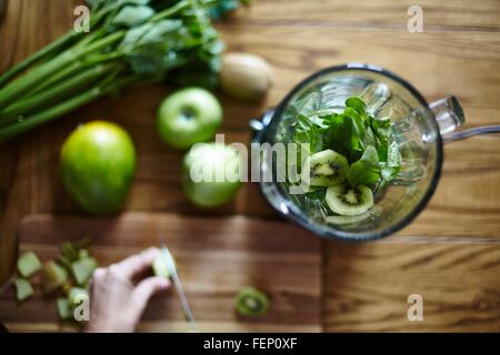 Woman cutting green kiwi on wooden table Stock Photo