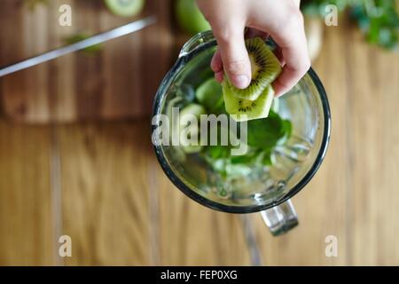 Woman holding sliced green kiwi over blender Stock Photo