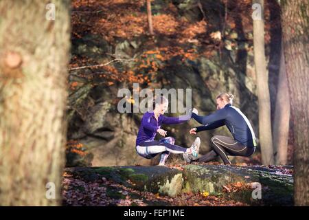 Side view of couple on rocks in forest face to face, holding hands, squatting balancing on one leg Stock Photo