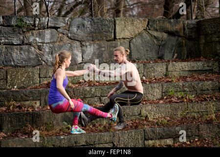 Side view of couple squatting on stone steps, face to face holding hands balancing on one leg Stock Photo
