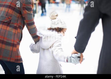 Rear view of girl ice skating with parents, holding hands Stock Photo