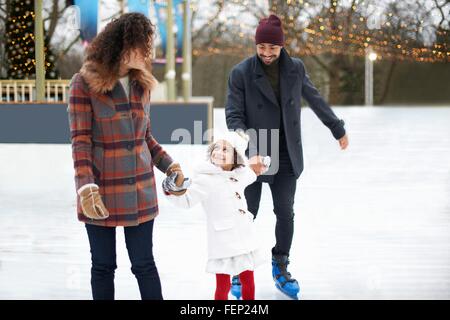Girl ice skating, holding hands with parents looking up smiling Stock Photo