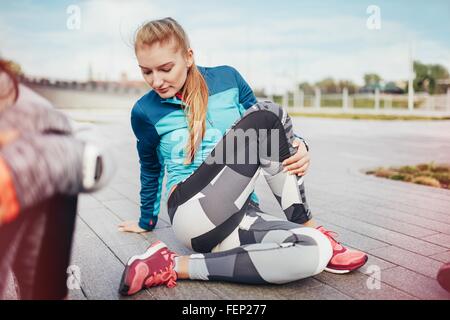 Female runners doing warm up stretches on pier Stock Photo