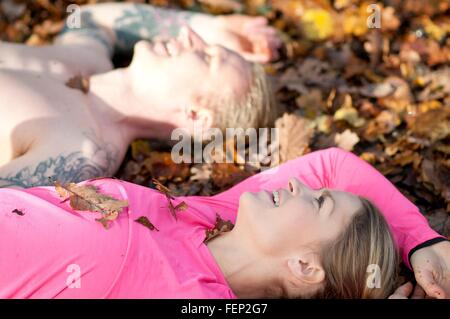 Side view of couples head and shoulders lying on autumn leaves looking up smiling Stock Photo