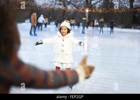 Girl on ice rink, arms open skating to mother smiling Stock Photo