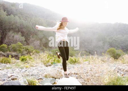 Young woman jumping on rock, smiling, outdoors Stock Photo