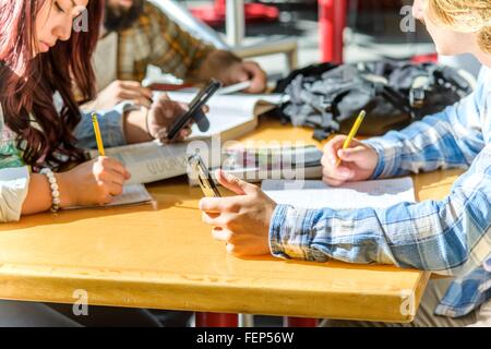 Cropped shot of college students using smartphones and writing at desk Stock Photo