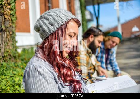 Adult college students reading books on campus wall Stock Photo
