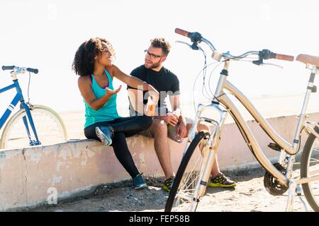 Couple sitting on wall, taking a break, bicycles beside them Stock Photo