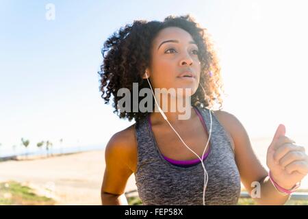 Mid adult woman running by beach, wearing earphones Stock Photo