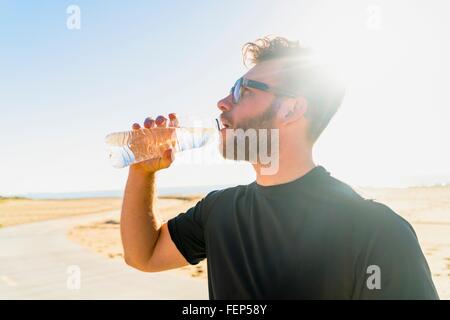 Young man, by beach, drinking from water bottle Stock Photo