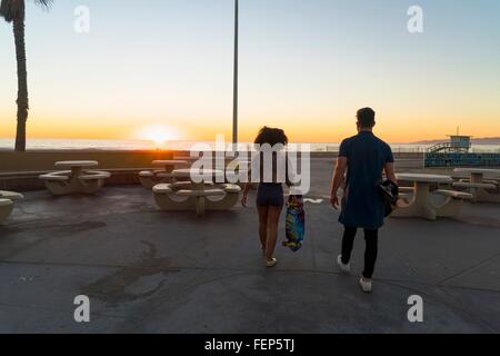 Couple walking near beach, holding skateboards, rear view Stock Photo