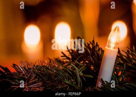 Electric Christmas light on a tree with candlelight in the background Stock Photo