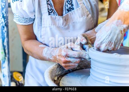 Close up of hands of female potter and mature student making pot on potters wheel Stock Photo