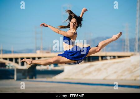Side view of young woman doing the splits in mid air looking at camera smiling, Los Angeles, California, USA Stock Photo
