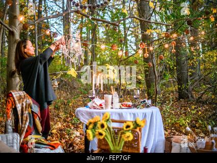 Mature woman hanging decorative lights in woods Stock Photo