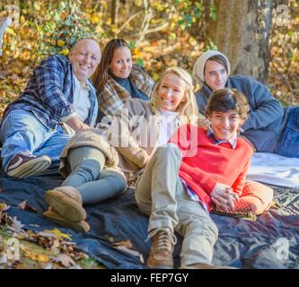 Portrait of mature couple with teenage and adult children relaxing on picnic blanket in woods Stock Photo