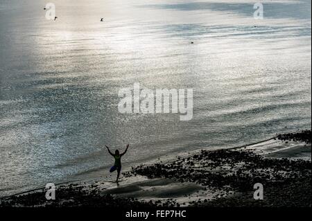 High angle silhouette of young woman practicing yoga standing tree pose on beach Stock Photo