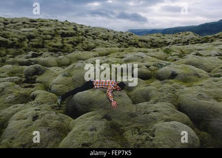 Side view of mid adult man lying on rolling volcanic landscape, Iceland Stock Photo