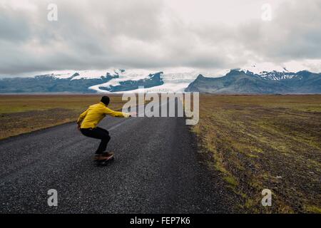 Rear view of mid adult man skateboarding to snow covered mountain range, Iceland Stock Photo