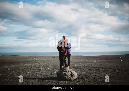 Mid adult couple standing on top of boulder on volcanic landscape, looking away, Iceland Stock Photo