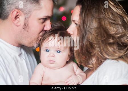 Mother and father face to face holding baby girl, kissing on head Stock Photo