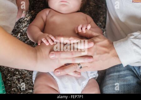 Overhead cropped view of mother and fathers hand on baby girls stomach Stock Photo