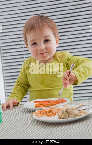 Baby boy feeding himself at dining table Stock Photo