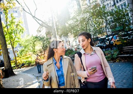 Young adult female twins chatting and walking through city park Stock Photo