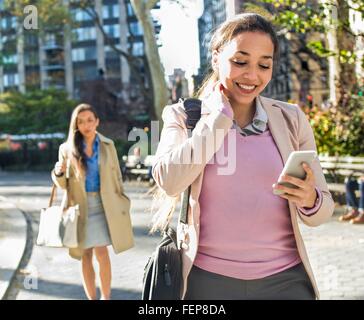 Young woman reading smartphone texts whilst walking through city park Stock Photo