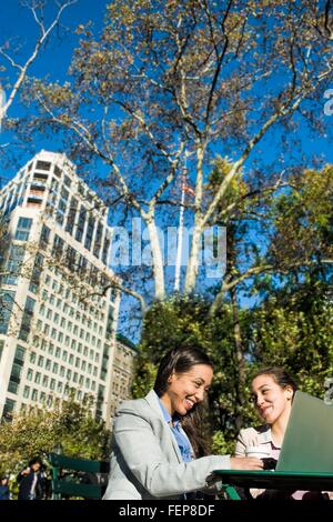 Young adult female twins using laptop in city park Stock Photo