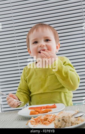 Baby boy feeding himself at dining table Stock Photo