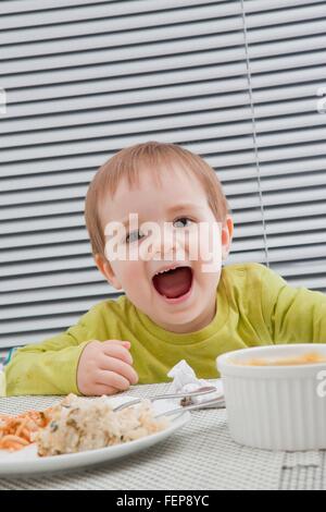 Baby boy feeding himself at dining table Stock Photo