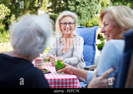 Three women sitting in garden, enjoying drink Stock Photo