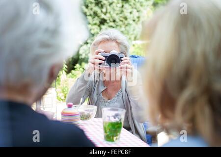 Senior woman, taking photograph of friends in garden Stock Photo