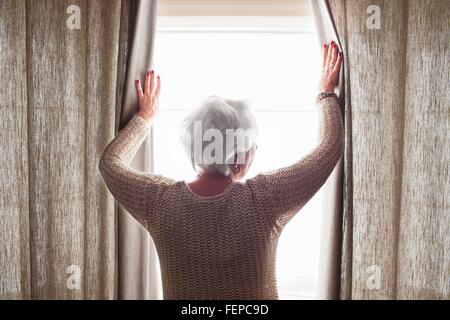 Senior woman, opening curtains, rear view Stock Photo