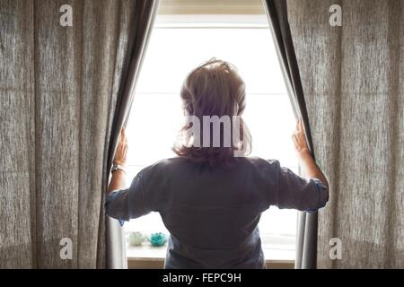Senior woman opening curtains, rear view Stock Photo