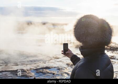 Woman photographing The Great Geysir, a geyser in the Haukadalur valley on the slopes of Laugarfjall hill, South West Iceland Stock Photo