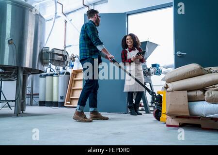 Colleagues in brewery using digital tablet and pallet jack smiling Stock Photo