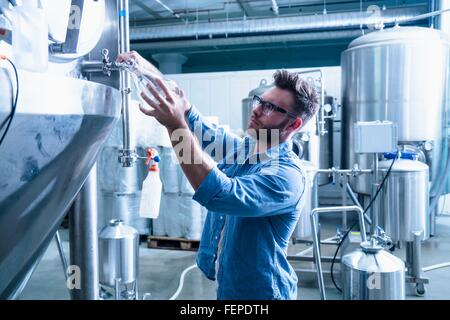 Young man in brewery filling flask with beer Stock Photo