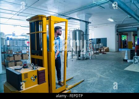 Young man in brewery driving forklift truck, looking away Stock Photo