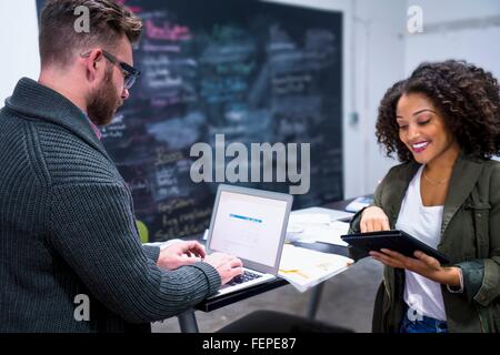 Colleagues in workplace using digital tablet and laptop smiling Stock Photo