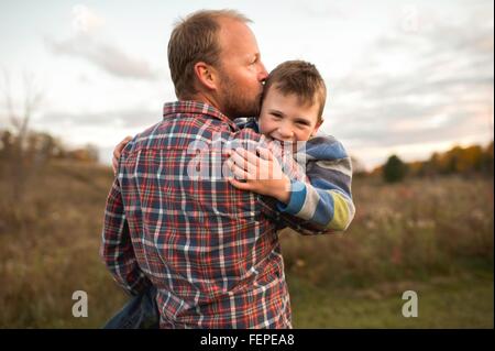 Rear view of father carrying smiling son, kissing him on forehead Stock Photo