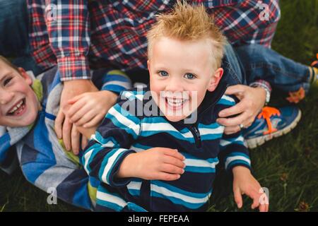 High angle view of father and sons in a huddle lying on grass looking at camera smiling Stock Photo