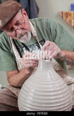Potter wearing flat cap finishing shaping clay vase, looking down Stock Photo