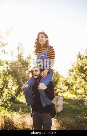 Young couple in rural environment, young woman sitting on man's shoulders, laughing Stock Photo