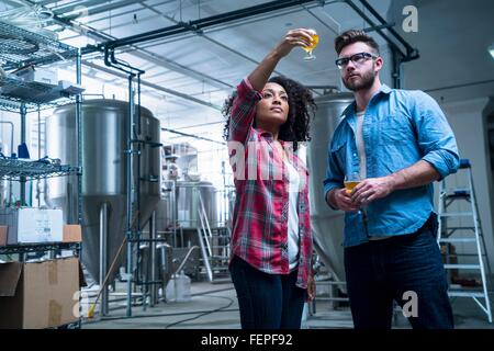 Colleagues in brewery holding up glass of beer, checking quality Stock Photo